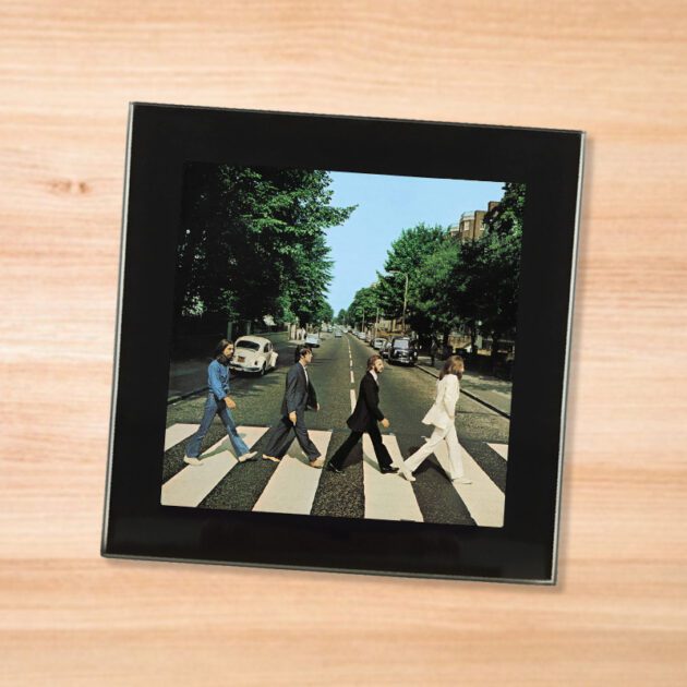 Black glass The Beatles - Abbey Road coaster on a wood table