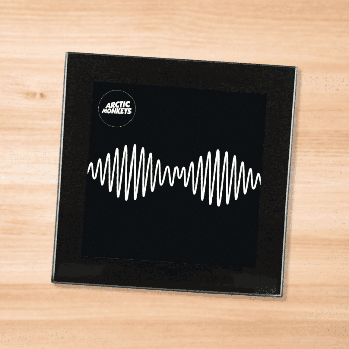 Black glass Arctic Monkeys album coaster on a wood table