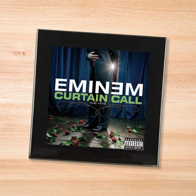 Black glass Eminem - Curtain Call coaster on a wood table