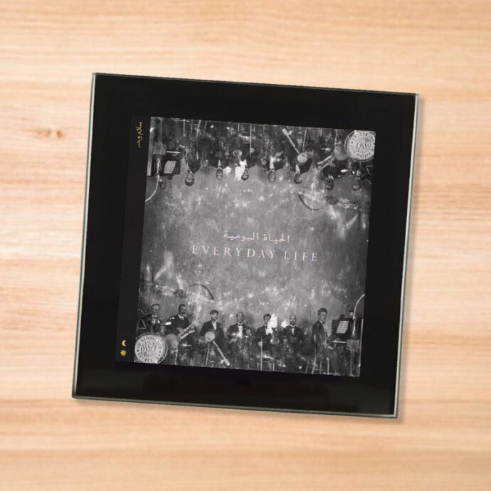 Black glass Coldplay - Everyday Life coaster on a wood table