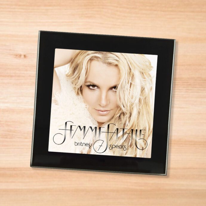 Black glass Britney Spears - Femme Fatale coaster on a wood table