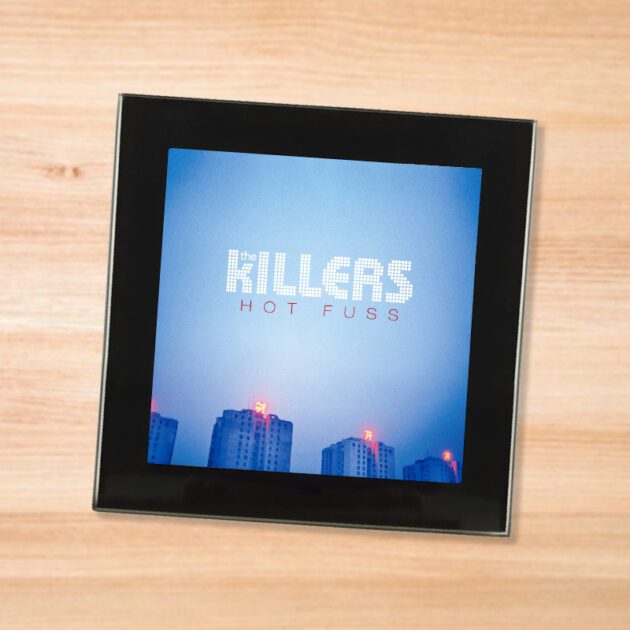 Black glass The Killers - Hot Fuss coaster on a wood table