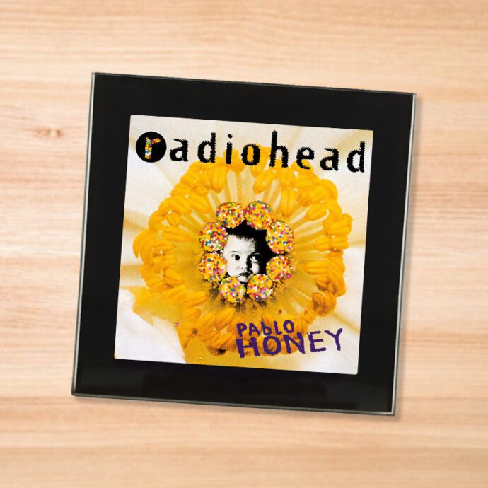 Black glass Radiohead - Pablo Honey coaster on a wood table