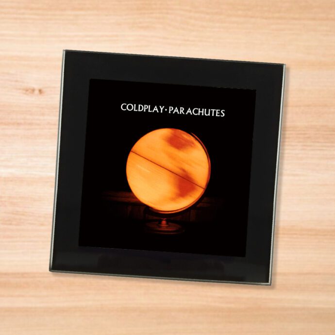 Black glass Coldplay - Parachutes coaster on a wood table