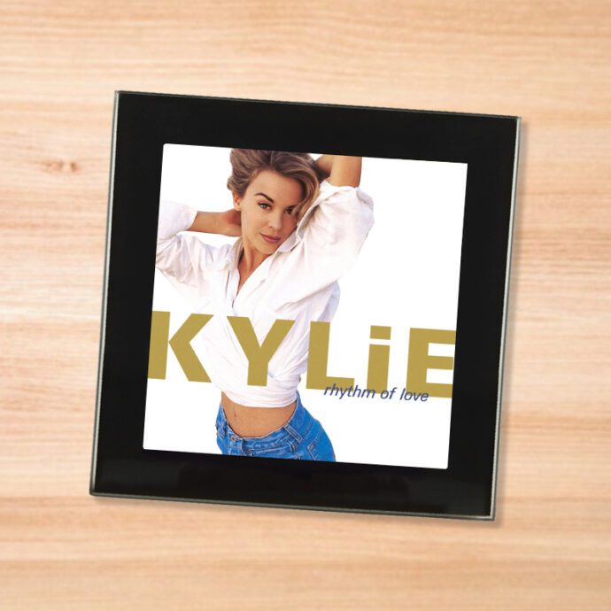 Black glass Kylie - Rhythm of Love coaster on a wood table