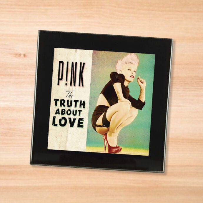 Black glass Pink - Truth About Love coaster on a wood table