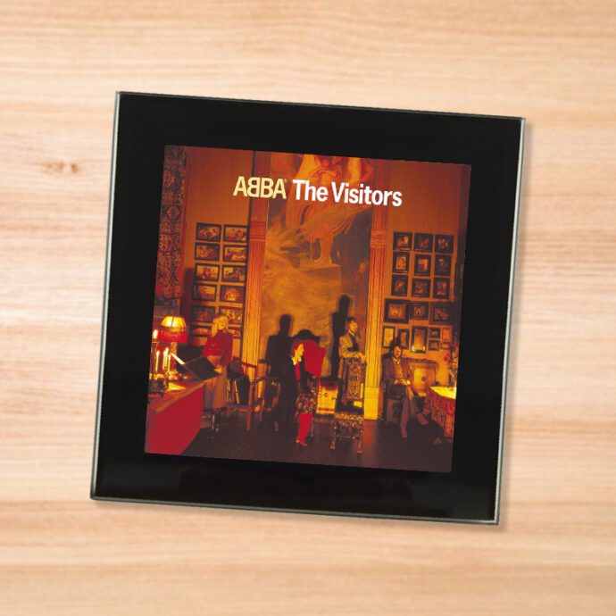 Black glass ABBA - The Visitors coaster on a wood table
