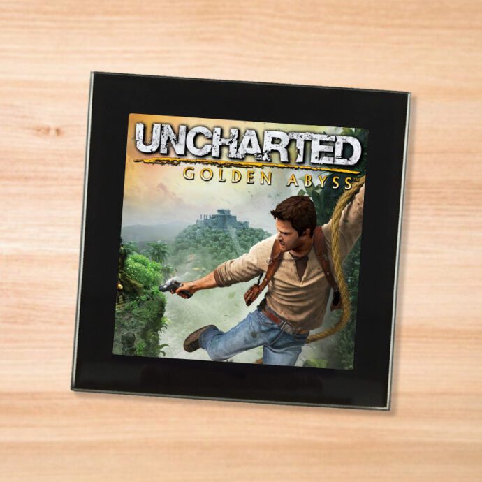 Black glass Uncharted Golden Abyss coaster on a wood table